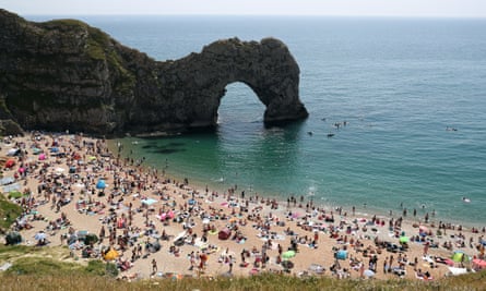 El conocido arco de piedra caliza de Durdle Door Beach, Dorset, y las personas que disfrutaron de la arena y el mar el sábado temprano.