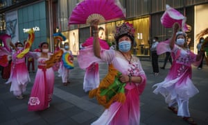 El 4 de junio de 2020 en Beijing, las mujeres chinas usan máscaras y trajes protectores mientras bailan para hacer ejercicio fuera de un centro comercial de lujo.
