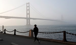 Una persona camina por el paseo marítimo cerca del puente Golden Gate, que está envuelto en una densa bruma en San Francisco.