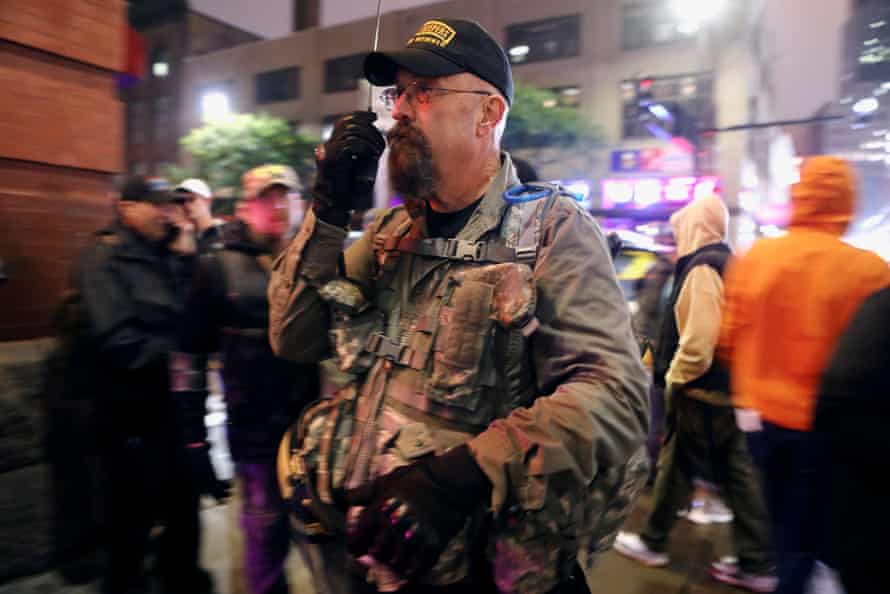 Un hombre con atuendo militar y una gorra de béisbol negra habla por radio mientras observa a la multitud.