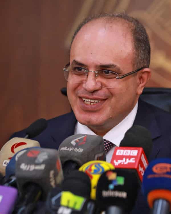 Un hombre sonriente rodeado de micrófonos durante una conferencia de prensa